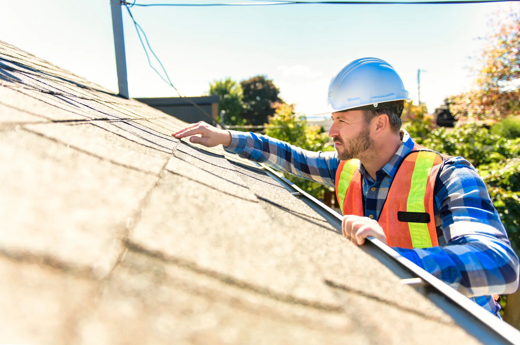 Roofing professional inspecting asphalt shingles on a residential roof.