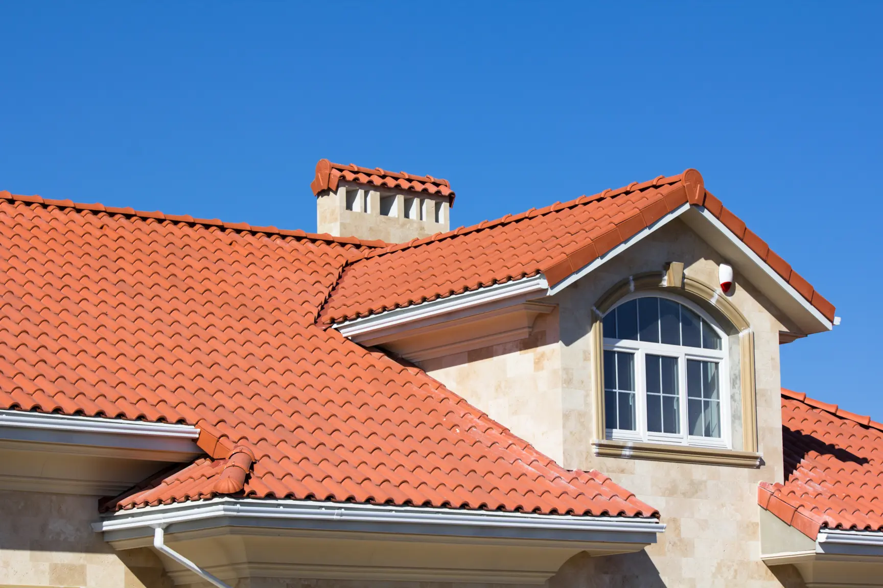 Red clay tile roof on a stucco home under a clear blue sky.