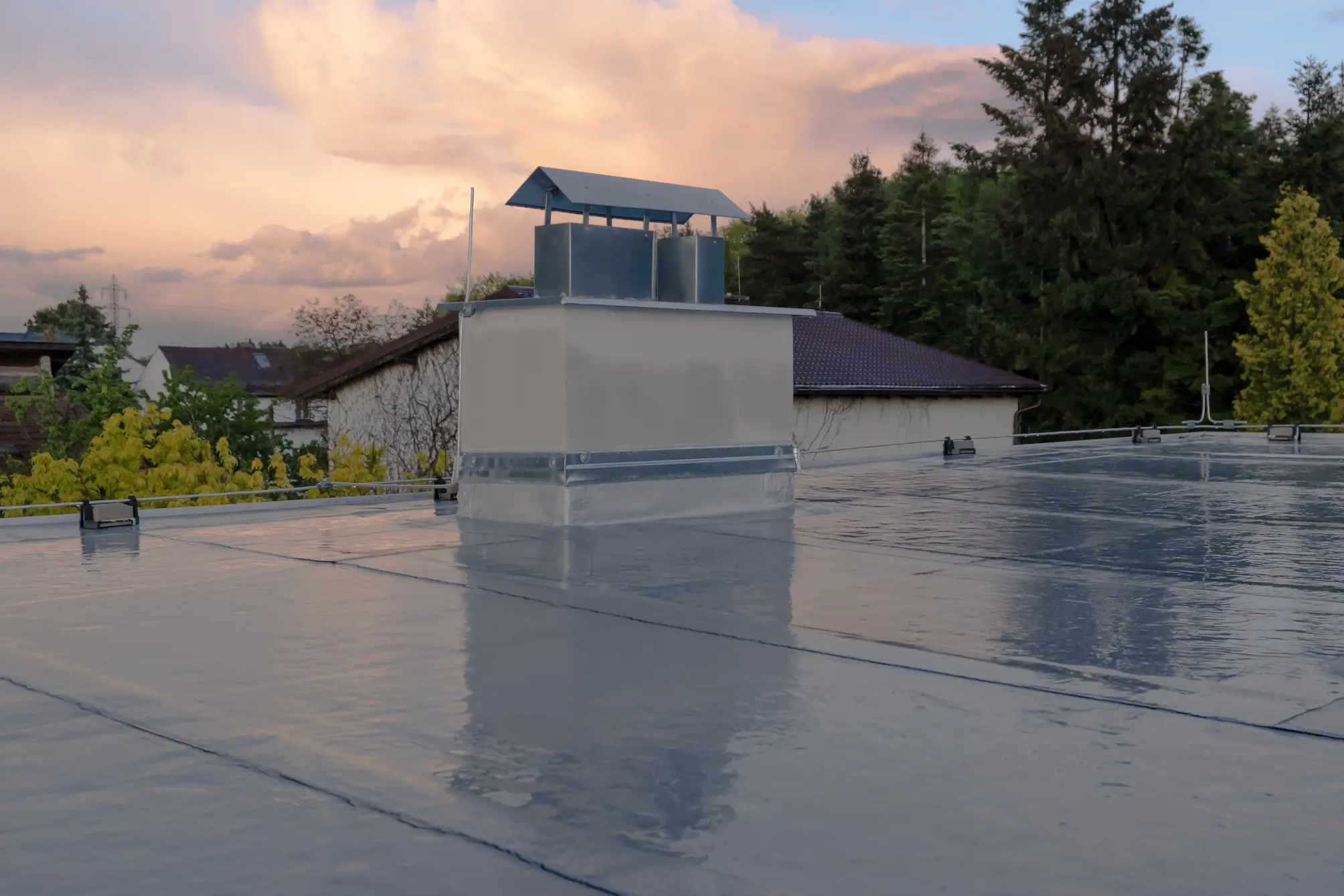 Reflective flat roof surface with a rooftop ventilation structure at sunset.