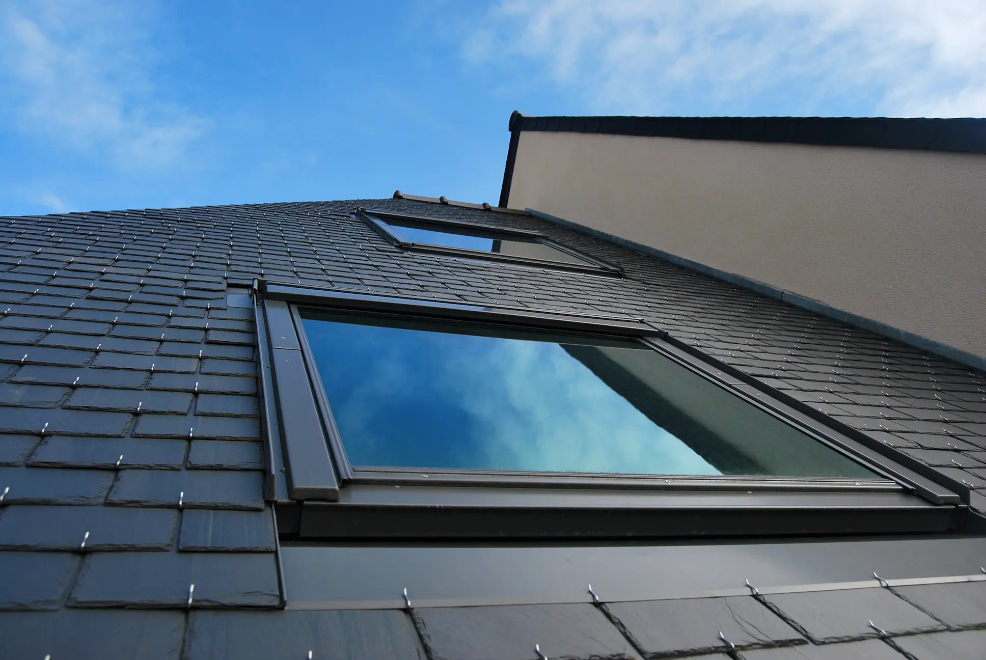 Dark slate roof with skylight windows on a steep residential roof.