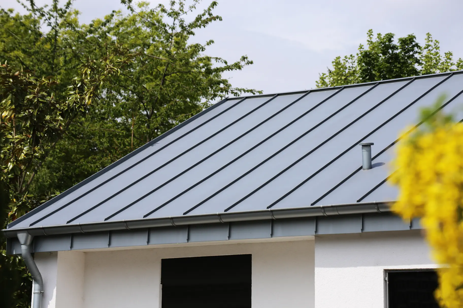 Standing seam metal roof on a modern residential home with trees in the background.